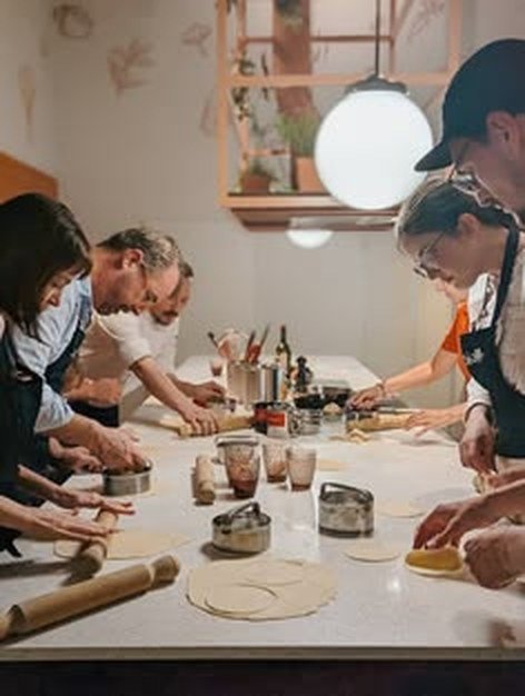 Guests gathered around a kitchen table rolling dough in a cooking class